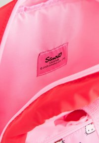 Doublure intérieure rose d'un sac avec une étiquette "Sanrio". Tissu lisse, fermeture éclair visible, accents imprimés présentant des designs de personnages.