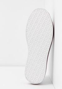 Podeszwa buta z teksturowanym gumowym gripem, z geometrycznymi wzorami. Kolor kontrastuje z ciemnym materiałem górnym i płaskim kształtem krawędzi.