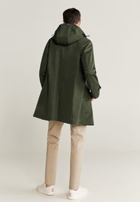 Vihreä hupullinen takki, väljässä istuvuudessa, valmistettu sileästä kankaasta. Yhdistetty vaaleanbeigeihin housuihin ja valkoisiin tennareihin, joissa on minimalistiset yksityiskohdat.