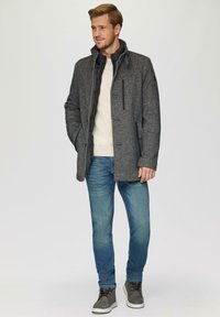 Grijze wolblend jas met een staande kraag, zwarte voering, voorzakken, grijs sweater eronder, blauwe spijkerbroek en grijze sneakers.