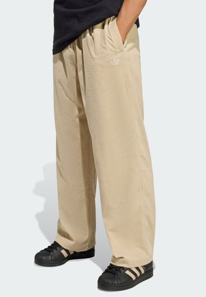 Beige corduroy pants with a relaxed fit, featuring front pockets and a small white logo on the left hip, paired with black sneakers.