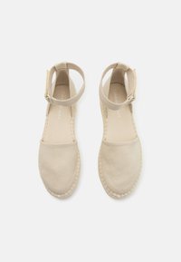Beige espadrillo sandaalit, joissa on kangas päällinen, nilkkahihna ja kudottu juuttipohja. Suuri pehmeä rakenne, pyöreä kärkitoteutus ja minimaalinen brändäys.