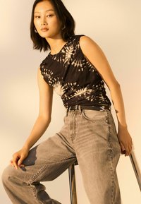 Zwart en crème tie-dye mouwloze top met rimpelingen; gecombineerd met lichtgrijze jeans. De outfit heeft een zwarte riem met een zilveren accent.