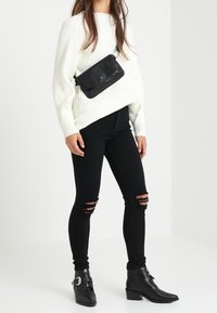 Vit ribbad tröja, svarta slitna slim fit jeans och svarta ankelstövlar med spännen. Svart axelremsväska accentuerar outfiten.