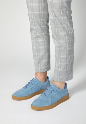 Lyseblå ruskindsneakers med rund tå, tekstureret overdel og gummisål. Bæres med grå ternede bukser, der er beskåret ved anklen.