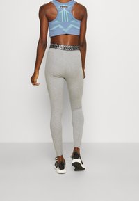 Grå leggings med en tætsiddende pasform, parret med en lyseblå sports-bh med et geometrisk mønster. Detaljer i sort og hvid ved taljen.