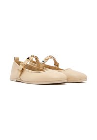 Bailarinas de piel beige con punta redonda, correas decorativas en el tobillo con acentos metálicos y una textura suave y lisa.