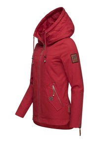 Chaqueta impermeable roja con capucha, que presenta bolsillos con cremallera, una tela texturizada con pequeños puntos y un parche con el logo en la manga.