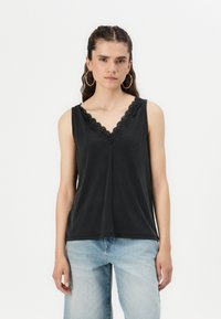 Top senza maniche nero con scollatura a V ondulata. Tessuto morbido, vestibilità rilassata, abbinato a jeans azzurri chiari, leggermente sfilacciati.