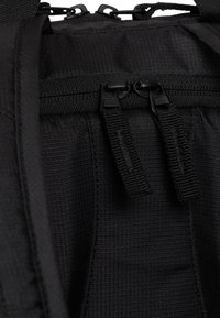 Czarne płócienne plecak zbliżenie ukazujące gładką fakturę, podwójne zamki błyskawiczne oraz taśmy wzmacniające zapewniające dodatkowe wsparcie i trwałość.