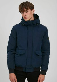 Navy blue puffer jacket with a hood, featuring two front pockets, adjustable toggles, and a ribbed hem and cuffs. Smooth texture, minimal design.