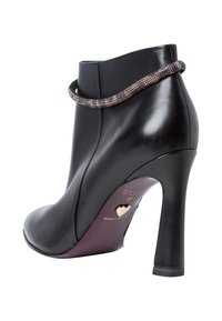 Svart läderankelboot med en svängd siluett, hög klack, prydd med ett pärlband och ett guldhjärtemblem på sulan.