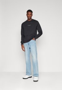 Felpa nera con logo, jeans in denim azzurro chiaro e zoccoli bianchi. Design semplice, vestibilità comoda, con dettagli a contrasto in texture.
