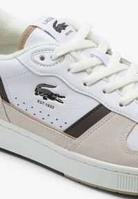 Sneaker bianca in pelle con accenti in suede beige, striscia marrone e logo in cocco nero. Presenta lacci bianchi testurizzati e linguetta imbottita.