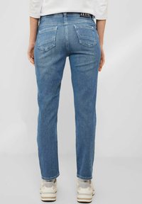 Jean en denim bleu clair avec une coupe droite, deux poches arrière et une étiquette de taille noire. Portés avec des baskets de couleur claire.