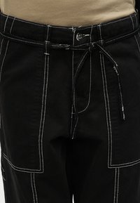 Μαύρο παντελόνι με λευκή ραφή, που διαθέτει ζώνη στη μέση, τσέπες τύπου patch και ανθεκτικό υλικό με μίγμα βαμβακιού. Εμφανές υφασμάτινο φινίρισμα.