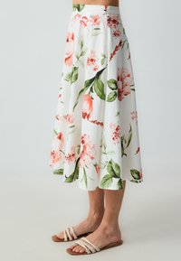 Weiße Blumenspitze Midi-Rock mit rosa und grünen Mustern. Leichter Stoff mit einem fließenden Design. Kombiniert mit beigen Riemchensandalen.