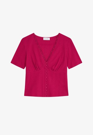 Blouse fuchsia à manches courtes, col en V, boutonnage sur le devant, légère fronce sous la poitrine et fines lignes verticales texturées.
