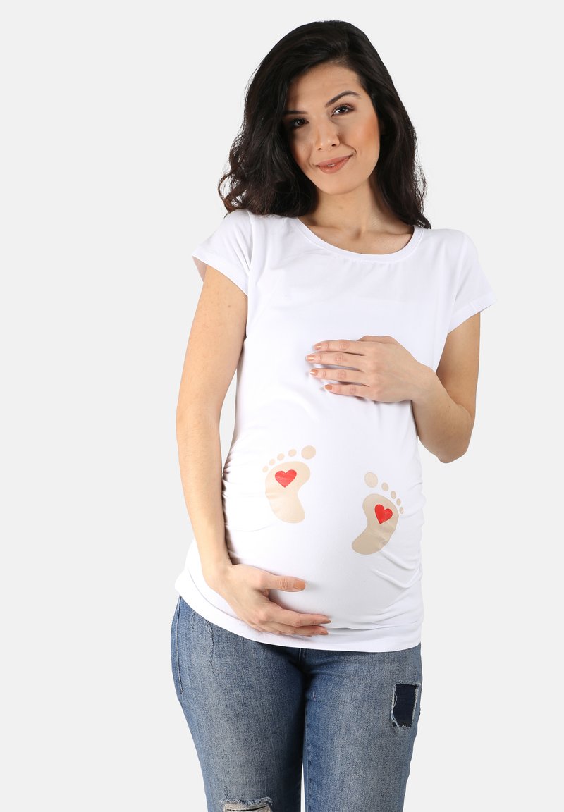 Weißes Maternity-T-Shirt mit kurzen Ärmeln, auf der Vorderseite mit beigen Babyfüßen und roten Herzen bedruckt, kombiniert mit lässigen blauen Jeans.