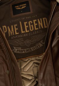Unutrašnjost smešnog kožnog jakna sa pamučnom podlogom. Značajno brendiranje izvezeno u zlatnoj i crnoj boji, sa krilima i natpisom "PME Legend."