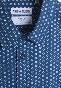 Camicia in cotone blu con una vestibilità slim, caratterizzata da un motivo geometrico bianco, colletto button-down e un singolo bottone blu nella parte anteriore.