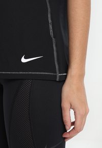 Svart atletisk linne med en sydd fåll och vitt Nike-logotyp. Matchat med svarta leggings med texturerade paneler och en elegant design.