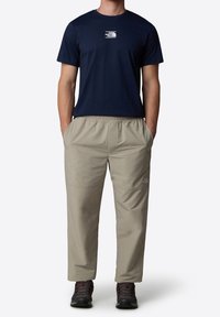 Mörkblå t-shirt i bomull med en vit logotyp på bröstet, i kombination med ljusbeiga byxor med elastisk midja och svarta kängor.