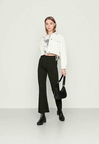 Jaqueta de ganga branca cortada sobre uma blusa tie-dye, combinada com calças pretas largas e botas pretas de combate. Uma bolsa preta completa o look.