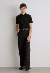 Schwarzes Polohemd und passende Hose, beide aus glattem Stoff. Das Outfit wird mit einem schwarzen Gürtel und glänzenden schwarzen Schuhen kombiniert.