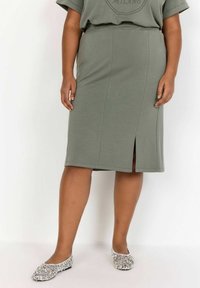 Faldă midi verde măsliniu dintr-un material moale, cu o deschidere pe lateral, asortată cu balerini din sequins argintii. Design simplu, cu un talie elastică.