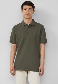 Olivgrünes Poloshirt mit klassischem Kragen, Drei-Knopf-Leiste, kurzen Ärmeln und kleinem Logo auf der linken Brust. Der Stoff scheint strukturiert zu sein.