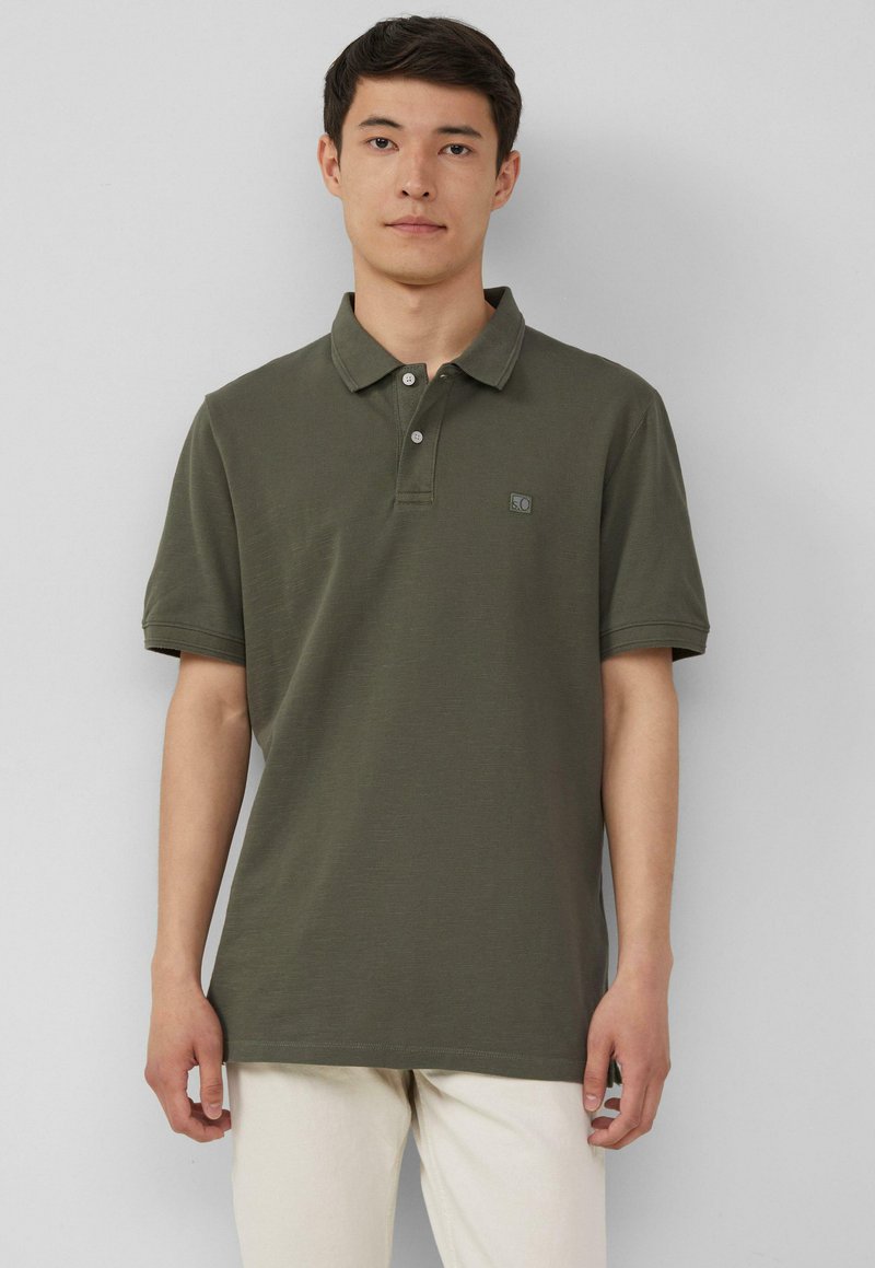Olivgrünes Poloshirt mit klassischem Kragen, Drei-Knopf-Leiste, kurzen Ärmeln und kleinem Logo auf der linken Brust. Der Stoff scheint strukturiert zu sein.