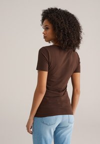 Bruin T-shirt met korte mouwen en een getailleerd ontwerp, zachte textuur en een ronde hals, gecombineerd met lichtblauwe spijkerbroek.