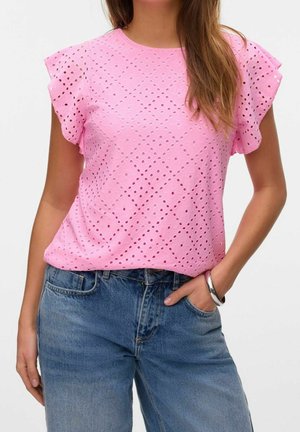 Femme portant un chemisier rose à manches courtes avec un motif œillet, associé à un jean bleu et un bracelet argenté au poignet droit.