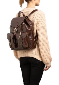 Zaino in pelle marrone con pattina superiore, due tasche frontali e dettagli in metallo. Texture liscia con un design robusto e spallacci regolabili.