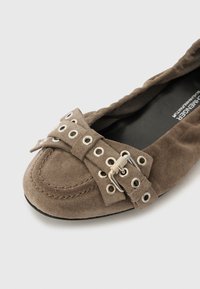 Suede flate sko i taupe med en sløyfe med sølvøyellets og et spenne. Rund tå og sydd kant. Glatt indre fôr.