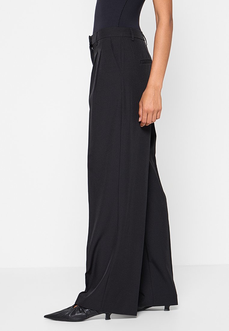 Pantaloni neri a gamba larga realizzati in tessuto liscio, con vita alta, passanti per la cintura e due tasche laterali per un look sartoriale.
