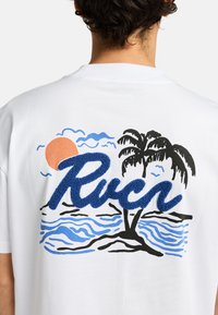 Hvid t-shirt med et farverigt grafisk print af en solnedgang, palmer, bølger og blå tekstureret "Rvca" bogstaver på ryggen.