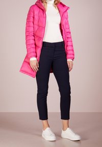 Różowa kurtka puchowa z kapturem, o pikowanej teksturze; noszona na białym golfie, w połączeniu z granatowymi spodniami i białymi butami.