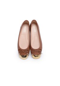 Zapatos planos marrones con una textura suave, detalle de lazo en la parte delantera y puntera dorada brillante. El interior es de un color beige claro con marca.