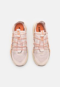 Ljusrosa sportskor med texturerat mesh-övre, elastiska bungee-snören, orange detaljer och en robust beige sula för grepp.