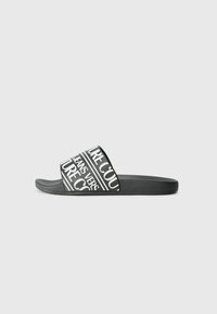 Sandale noire à talon plat avec un semelle texturée et une large sangle ornée de motifs en texte blanc en gras. Construction légère pour un confort optimal.