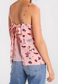 Blusa floreale rosa con sottili spalline, schiena aperta legata con un fiocco, caratterizzata da una vestibilità ampia e un motivo botanico in tonalità di rosso e blu.