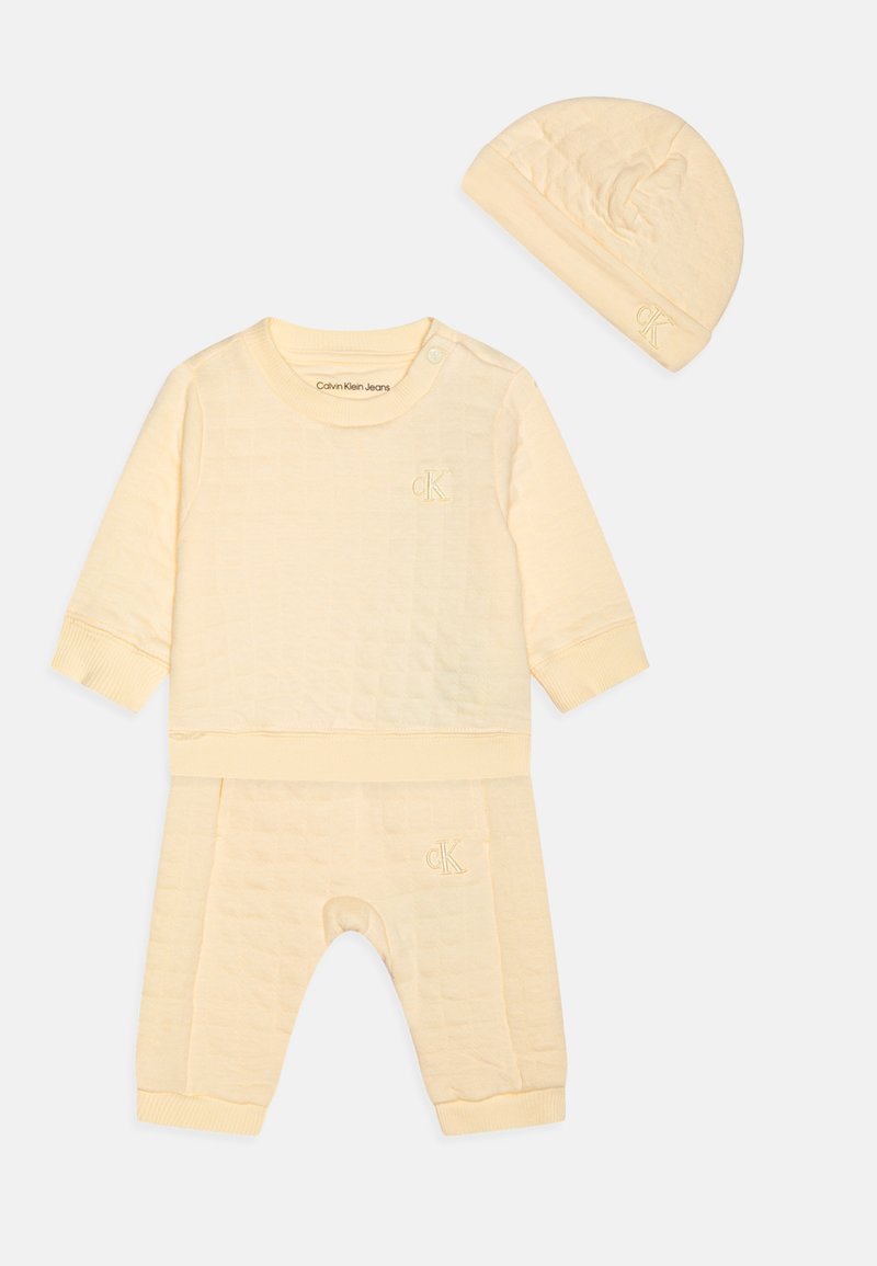Rumena prešita otroška obleka, sestavljena iz dolgosleeve majice z gumbom na pritisnitev, ujemajočih hlač in kapa, vse z vezenimi logotipnimi detajli.