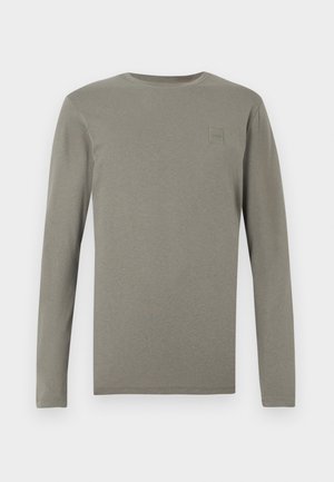 Pitkähihaisen paidan väri on hillitty oliivinvihreä, valmistettu pehmeästä puuvillasta, jossa on pyöreä pääntie ja pieni neliölogolla rintamuksessa.