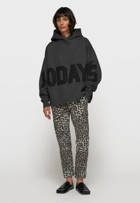 Grauer übergroßer Hoodie mit fettem schwarzen "100DAYS"-Schriftzug, kombiniert mit engen Leggings im Leopardenmuster. Glatte Textur und dunkle Slipper.
