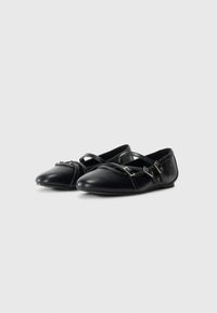 Un paio di scarpe flat in pelle nera con punta affusolata e doppie cinghie con fibbia, esposte su uno sfondo bianco semplice.