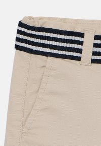 Pantalon en tissu beige avec une finition texturée, doté d'une taille élastique rayée bleu marine et blanc ainsi que de poches latérales.