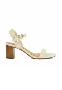 Sandale à talon beige avec une large bride avant, une bride de cheville ajustable et un talon en bois, comportant un détail de nœud décoratif.