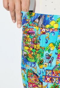 F ärgglad tyg med en design av en medelhavsby, med pastellfärgade hus, livfulla blommor och detaljerade mönster på en blå bakgrund.